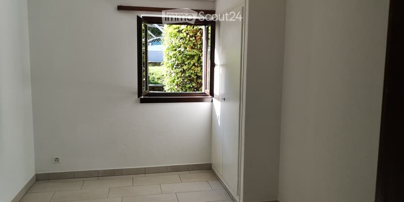 Empty room with tiled floor, white walls, and a window with wooden frame showing greenery outside.