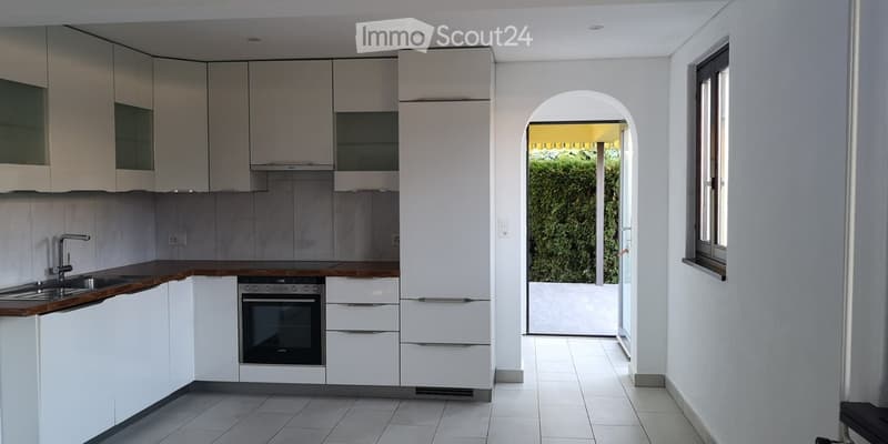 Modern kitchen with white cabinets, wooden countertops, stainless steel sink, and built-in oven. An arched doorway leads to an outdoor area.