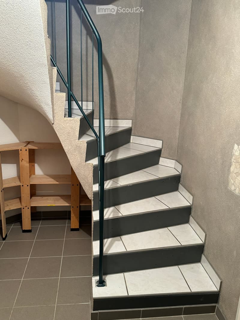 Staircase with modern design, featuring black and white tiles, a metal railing, and a wooden shelf on the side.