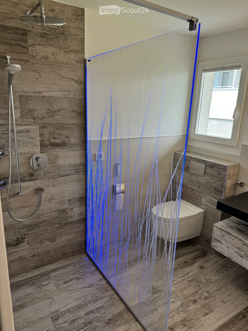 Modern bathroom with wooden walls and floor, glass shower enclosure with blue decorative lighting, toilet, and sink.