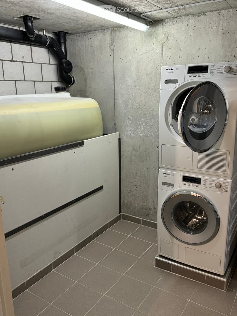 Utility room with a washing machine, water tank, and tiled floor.