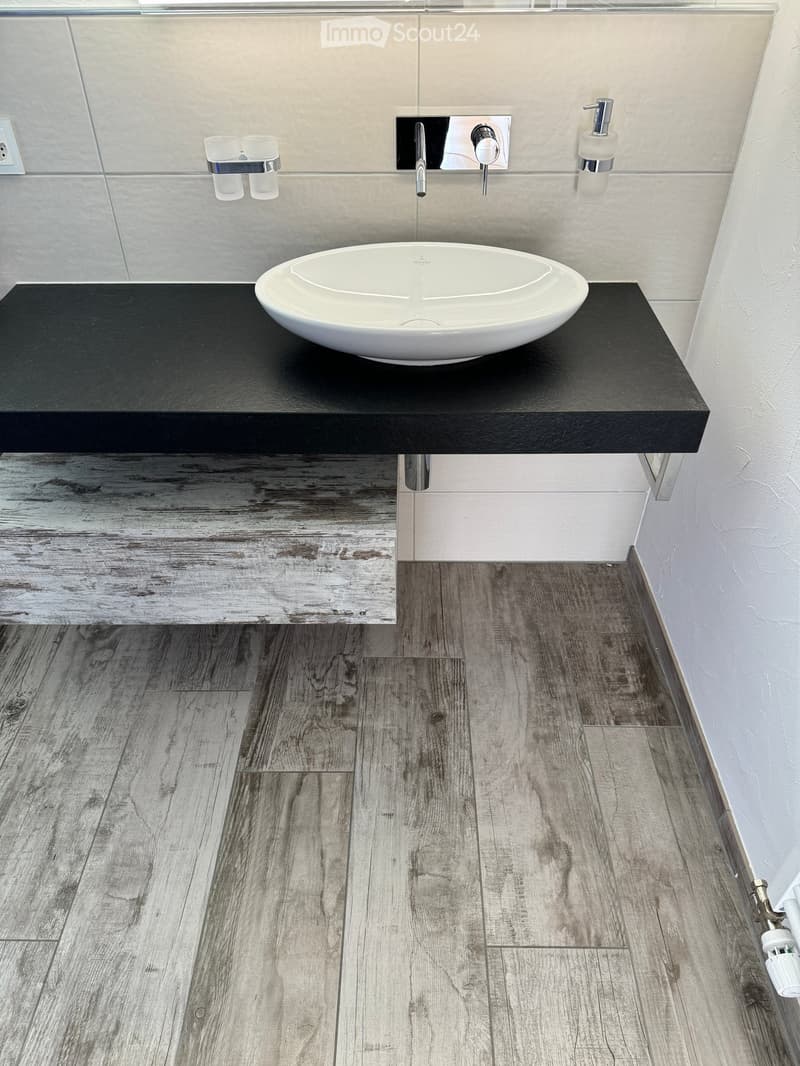 Modern bathroom with a sleek black countertop, a white sink, and a stylish faucet. The floor features a wood-like tile pattern.