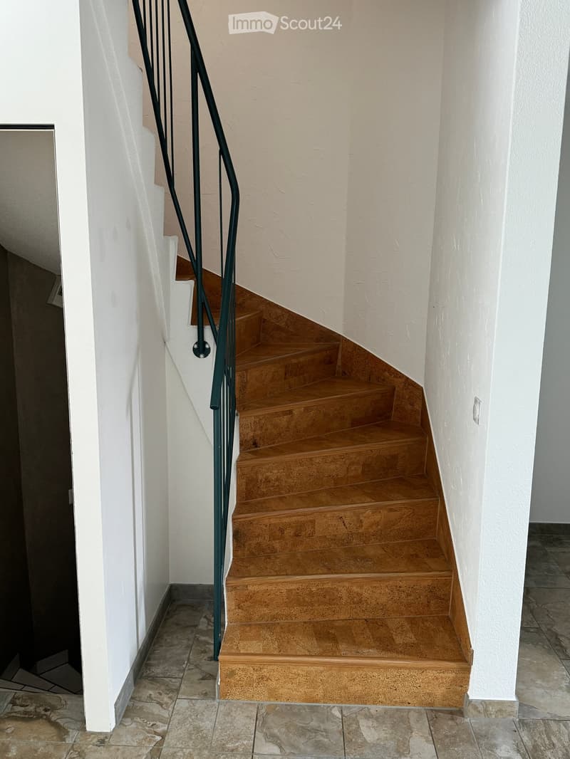 A staircase with wooden steps and a metal railing, leading upwards between white walls.