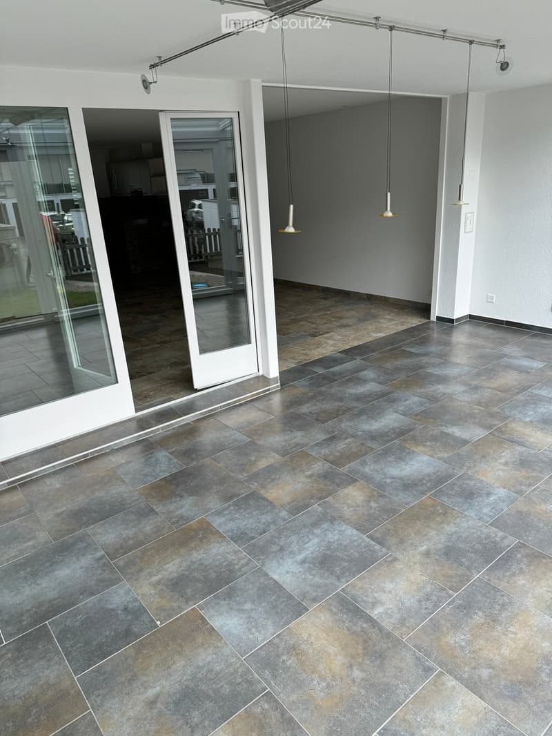 Modern balcony with grey tiled flooring, white sliding glass doors, and hanging pendant lights.