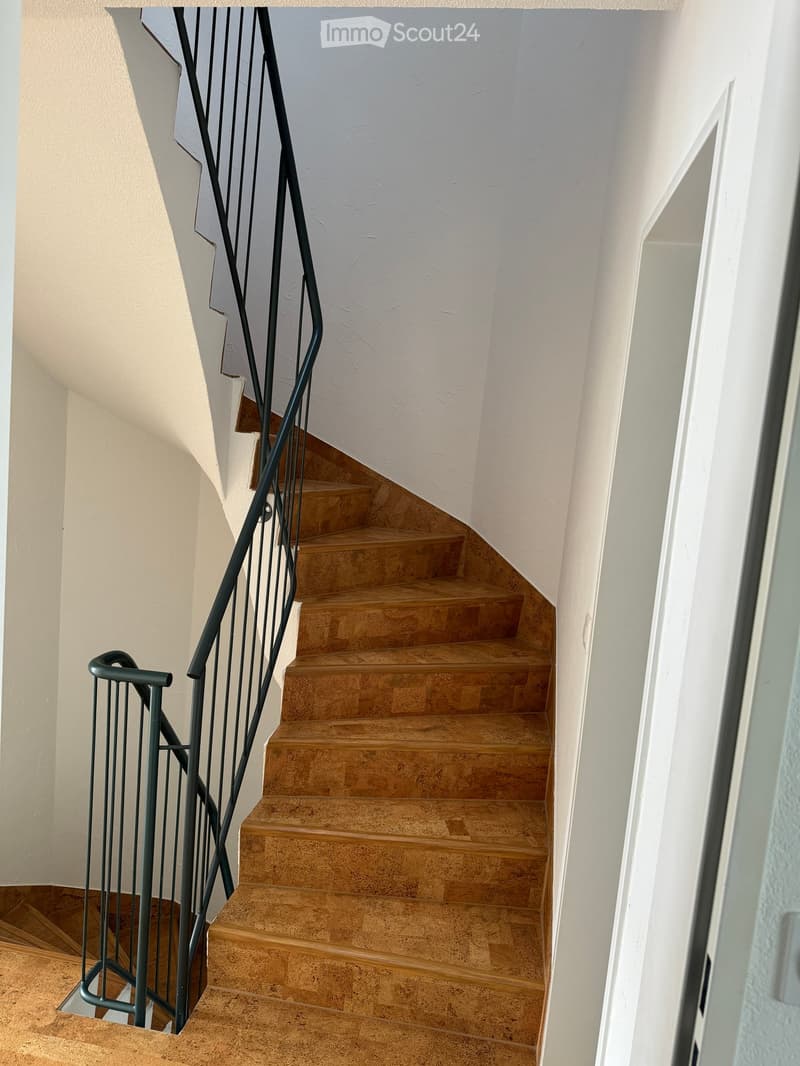A modern staircase with a sleek metal railing and warm-toned stone steps, leading upwards in a well-lit interior space.
