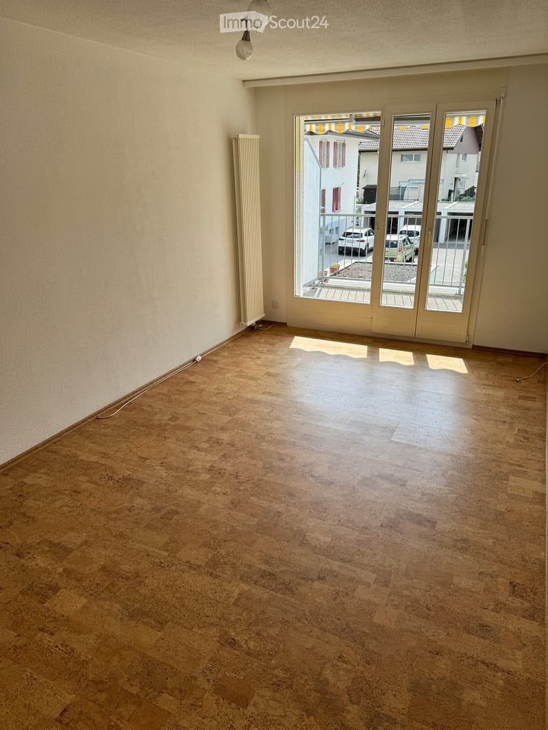 Empty room with wooden flooring, white walls, radiator, and large sliding glass doors leading to a balcony.