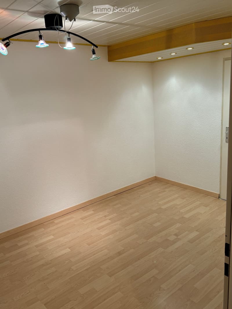 Empty room with light wooden flooring and white walls, featuring recessed ceiling lights and a track light fixture.