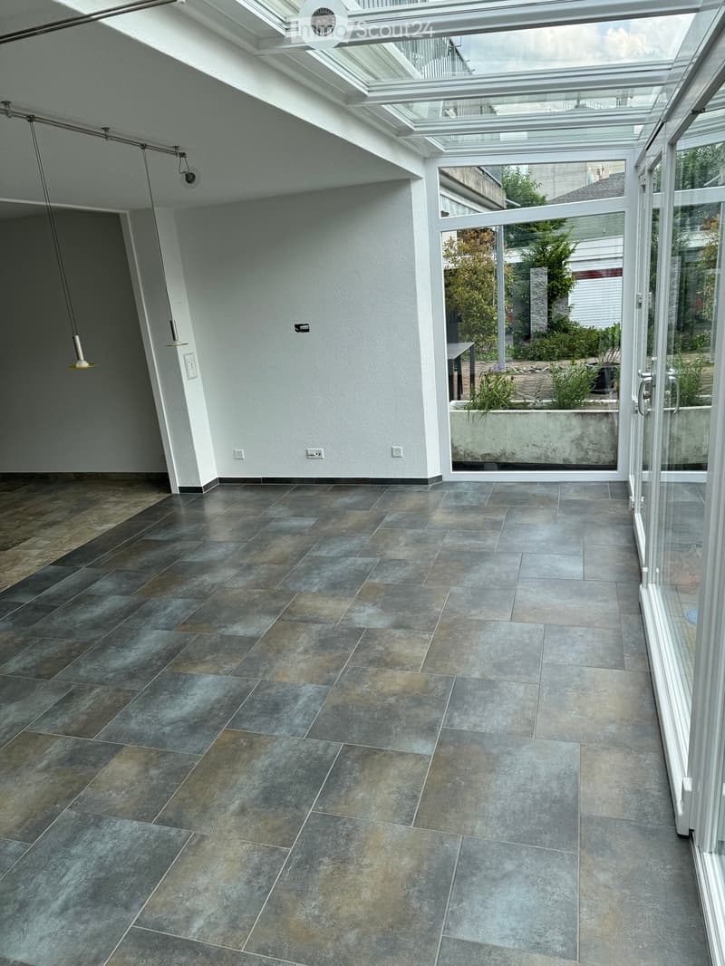 Empty room with large windows and a skylight, featuring a tiled floor and modern lighting fixtures.