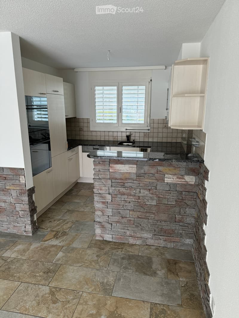 Modern kitchen with stone-tiled island, white cabinets, stainless steel sink, and oven.