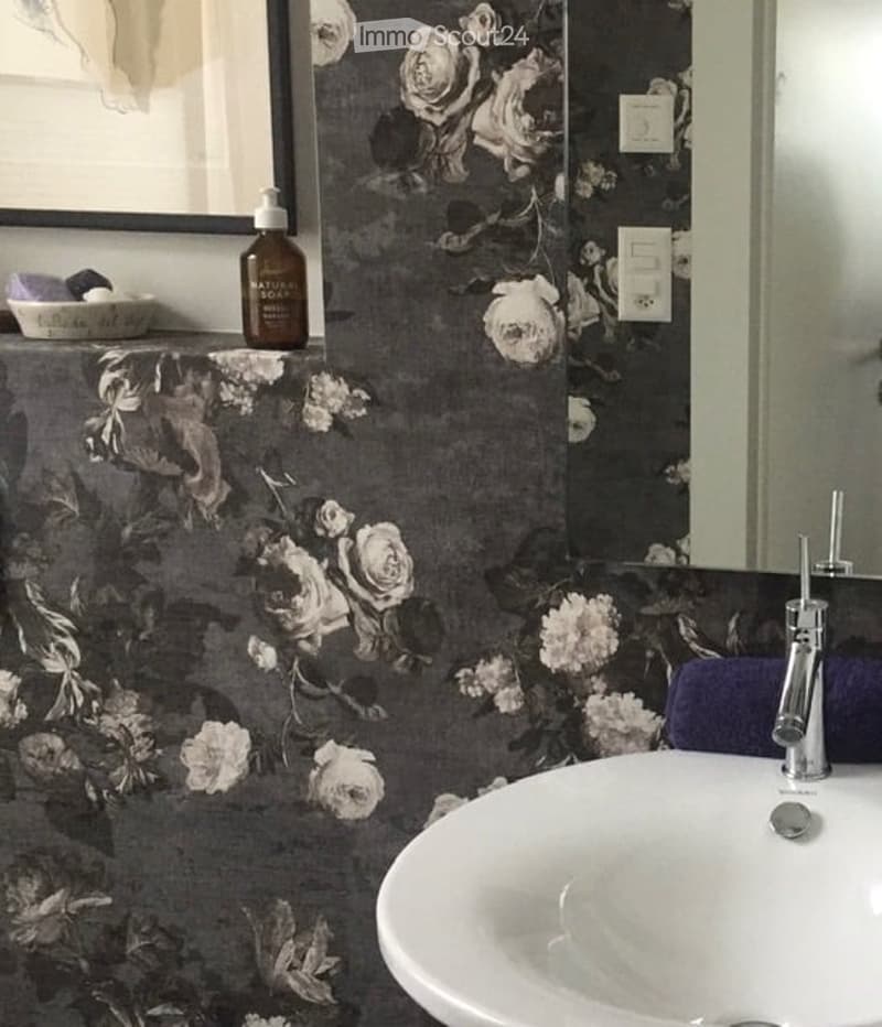 Bathroom with floral wallpaper, white sink, chrome faucet, and a bottle on the counter.
