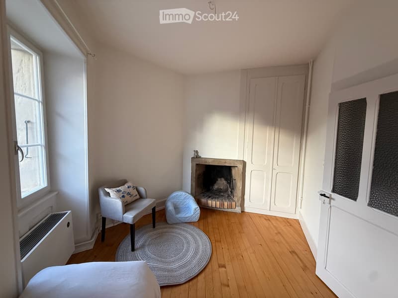 Cozy room with a fireplace, a sofa, a chair, a small bed, and a round rug on a wooden floor.