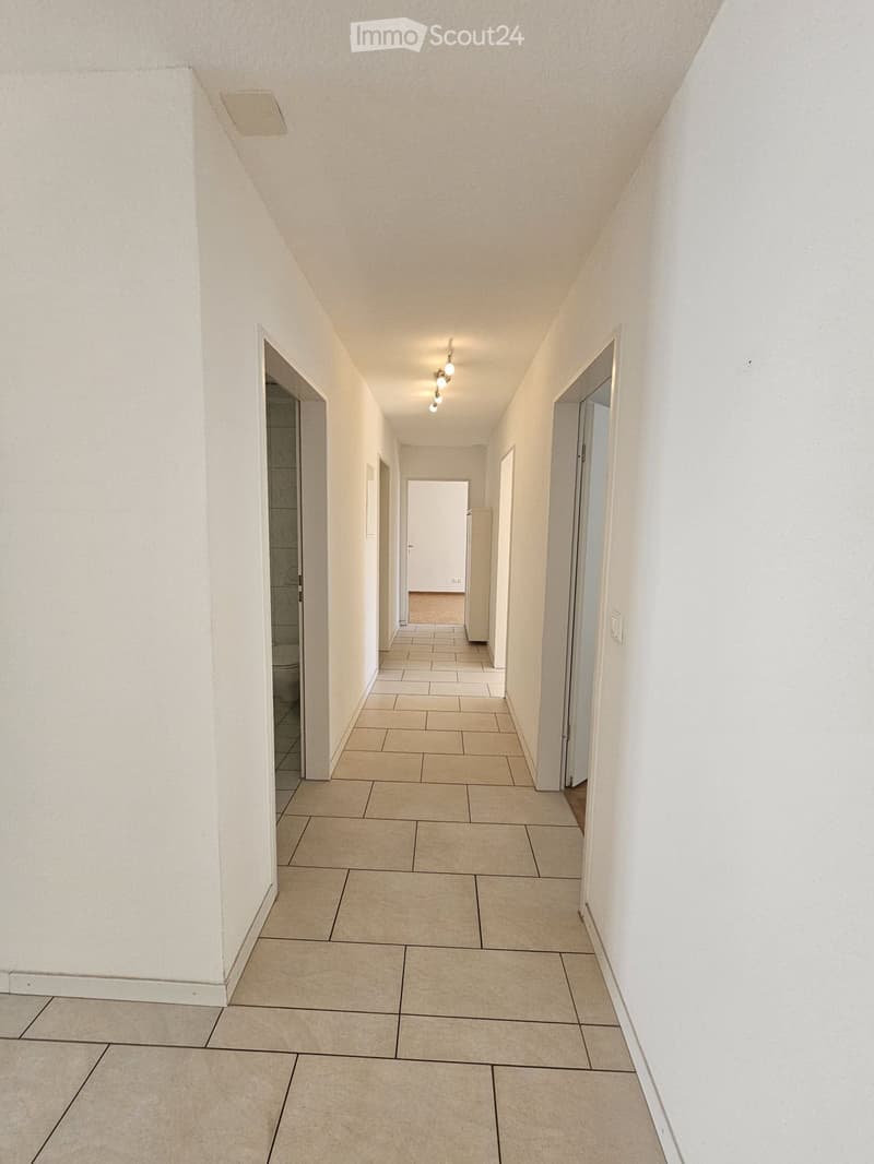 Empty hallway with tiled floor, white walls, and recessed lighting. Doors lead to adjacent rooms.