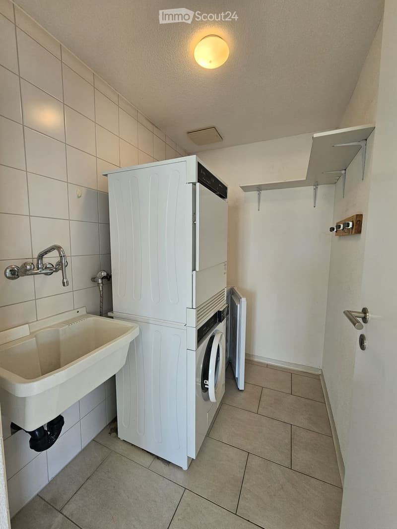 Clean bathroom with a white washing machine, a sink with a faucet, and tiled walls and floor.