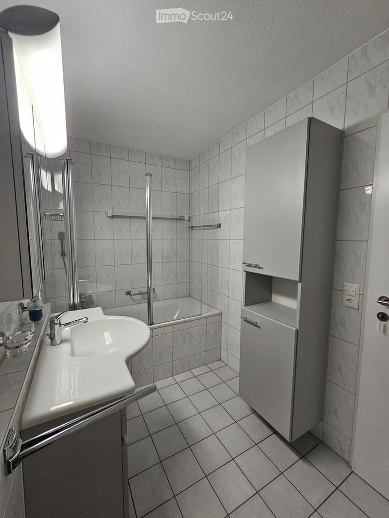 Modern bathroom with white tiled walls and floor, a white sink with a chrome faucet, a mirrored cabinet, and a glass-enclosed shower area.