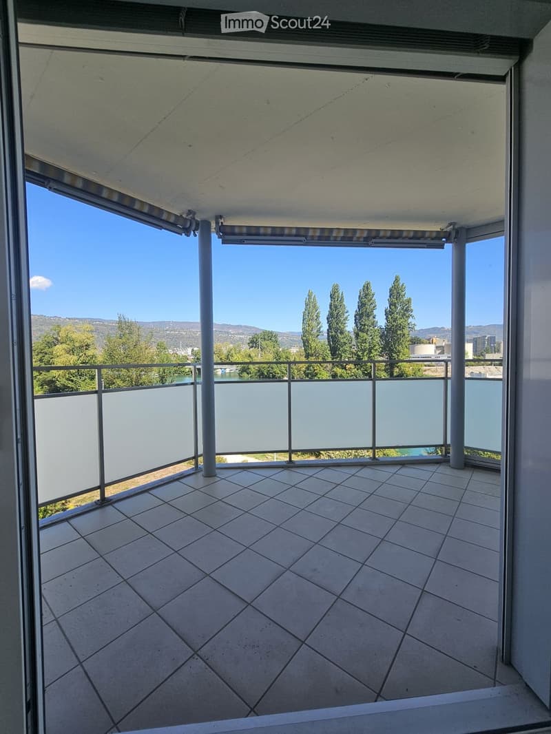 Balcony with tiled floor, metal railing, and a view of trees and a body of water.