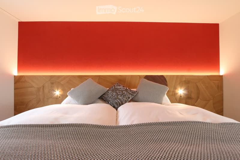 Modern bedroom with a large bed, wooden headboard, decorative pillows, and a textured blanket.