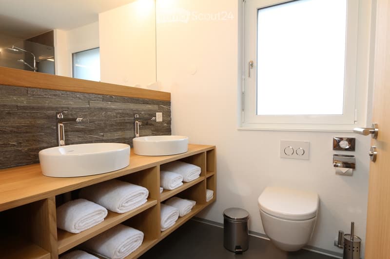 Modern bathroom with double sinks, wooden vanity, white towels, and a large window providing natural light.