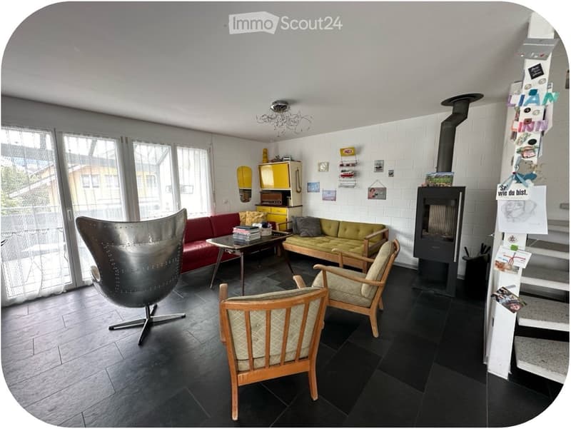 Living room with a fireplace, sofa, table, chairs, and a cabinet. The room features a modern aesthetic with a mix of wooden and metal furniture.