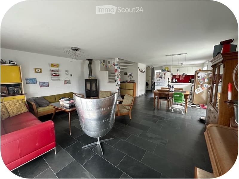 Open-plan living and dining area with a red leather sofa, coffee table, dining table with chairs, fireplace, and kitchen area with cabinets and appliances.