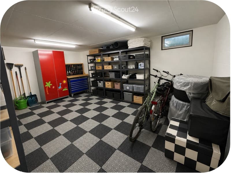 The image shows a well-organized utility or storage room with a black and white checkered floor. Visible items include a bicycle, shelves filled with storage bins and tools, a red toolbox, a broom and shovel, a small stool, and a covered object that appea