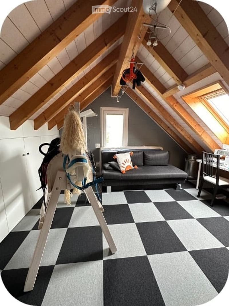 Attic room with exposed wooden beams, grey walls, black and white checkered floor, sofa, toy horse, and a small table.