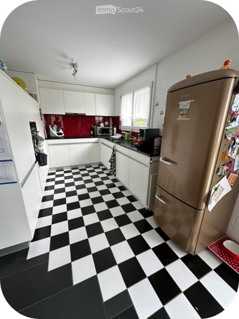 Modern kitchen with white cabinets, black and white checkered floor, stainless steel refrigerator, microwave, and oven. The countertops are black, and there is a red backsplash behind the stove.