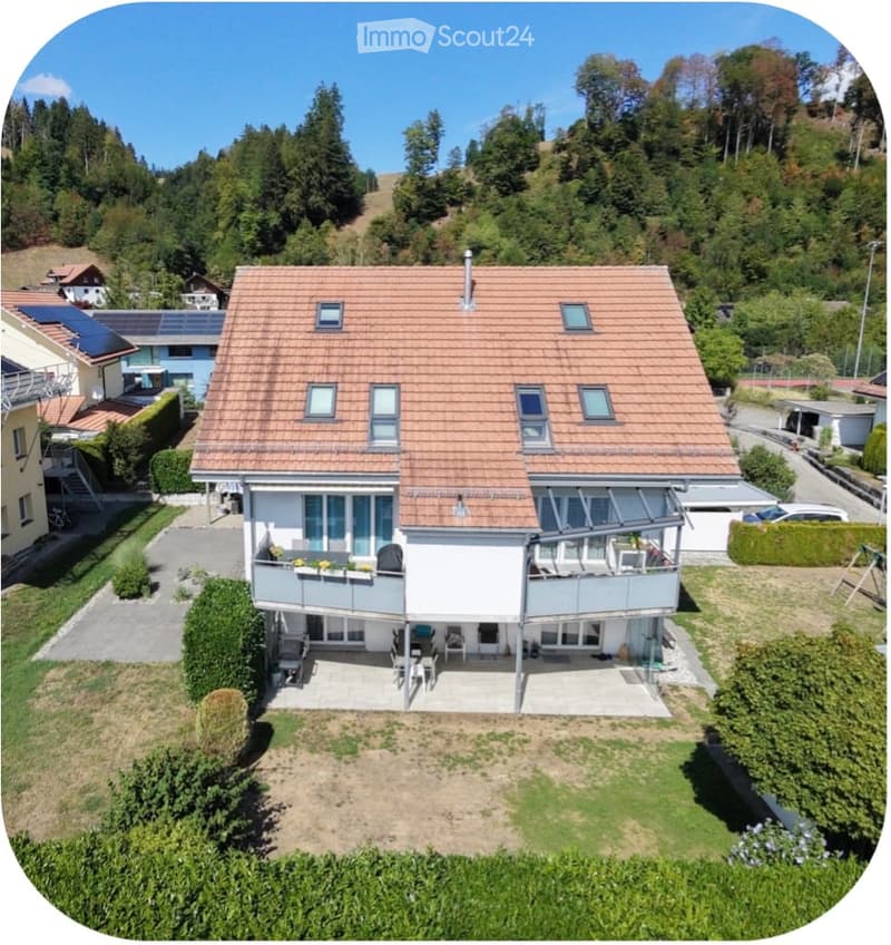 A two-story house with a red-tiled roof, multiple windows, and a balcony area with outdoor furniture.
