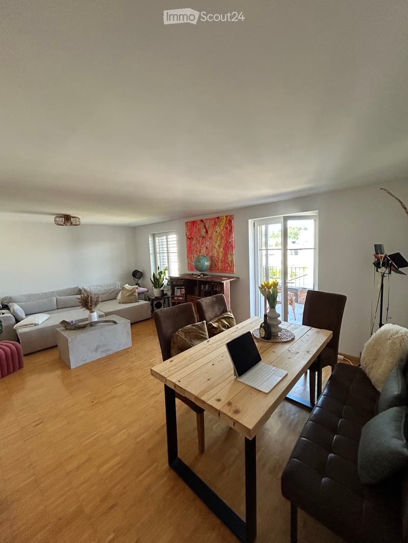 A modern living room with a wooden floor, a grey sofa, a coffee table, a laptop on a wooden table, and a leather armchair.