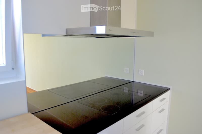 Modern kitchen with a sleek black induction cooktop, white cabinets, and a stainless steel range hood.