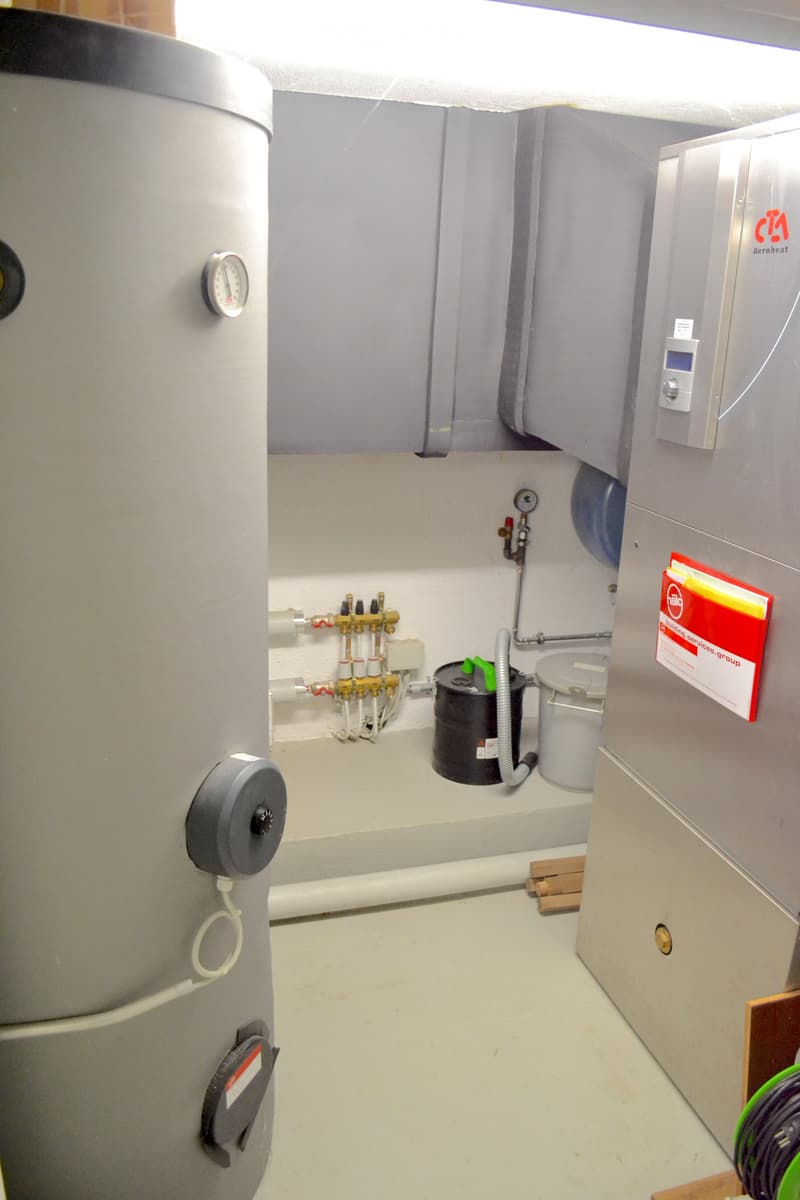 Utility room with water heater, control panel, pipes, valves, and a cylinder. Includes a cable and a small black container.