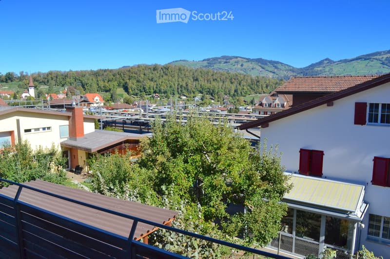 View of a residential area with houses, trees, and a distant mountainous landscape under a clear blue sky.