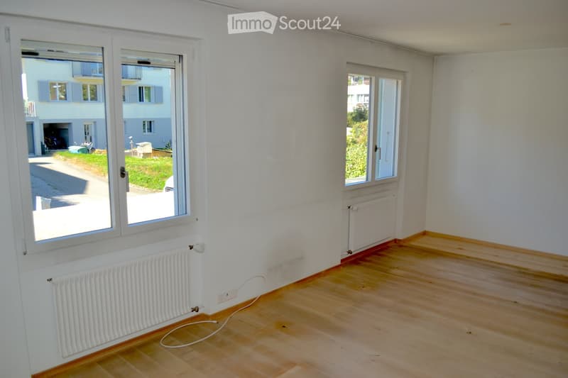 Empty room with wooden flooring, white walls, and large windows with radiators beneath them. The room is unfurnished and has a neutral color scheme.