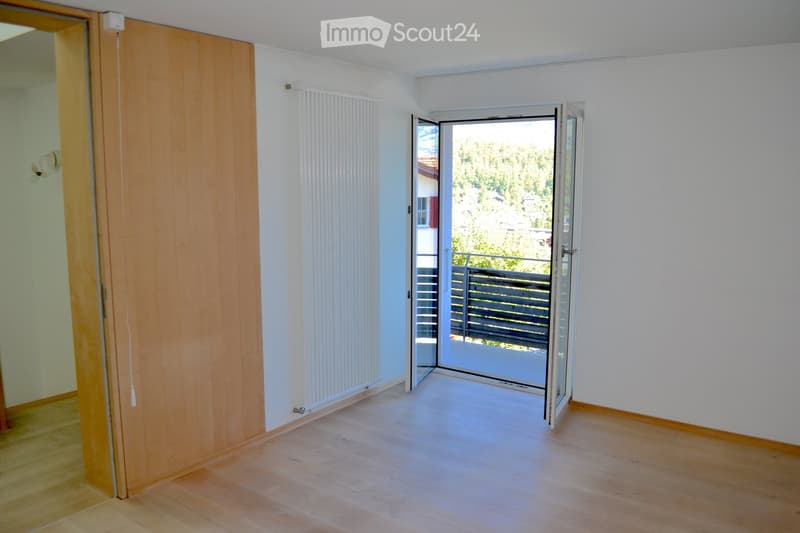 Empty room with wooden flooring, white walls, a sliding glass door leading to a balcony, and a radiator on one wall.