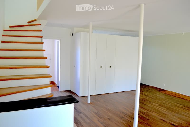 Empty hallway with wooden flooring, white walls, and a staircase leading upwards. Features a white closet and a white column.