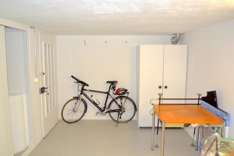 A small, unfurnished room with a bicycle, helmet, and a small table with a cup and a plastic bag on it.