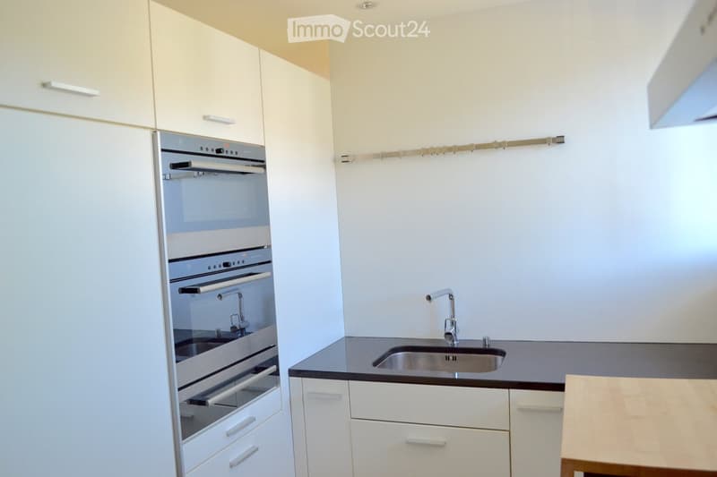 Modern kitchen with white cabinets, stainless steel sink, and built-in oven. Features a sleek black countertop and minimalist design.