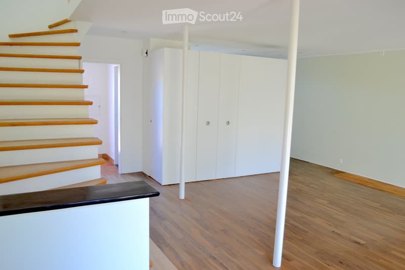 Empty room with wooden flooring, white walls, a staircase with wooden steps, and a white closet unit.