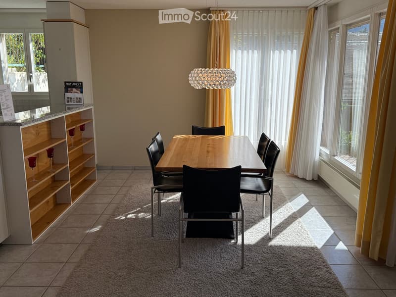 Dining room with a wooden dining table, six black chairs, a modern chandelier, and a wooden shelf with decorative cups.