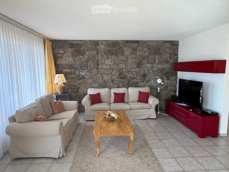 Living room with a stone accent wall, beige sofa, wooden coffee table, and a TV stand with a flat-screen TV.