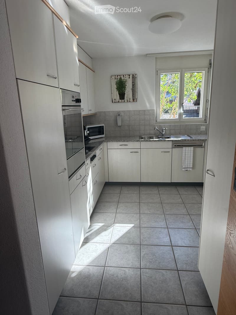 Modern kitchen with white cabinets, granite countertops, stainless steel appliances, and a large window letting in natural light.