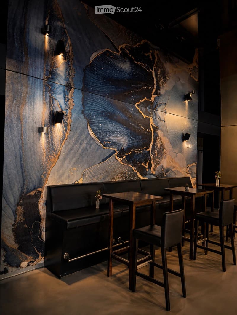 Modern interior with dark leather sofa, wooden tables, and chairs arranged around a central table, illuminated by wall-mounted spotlights.