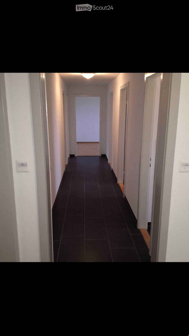 A corridor in a multistory building with tiled flooring, white walls, and doors.