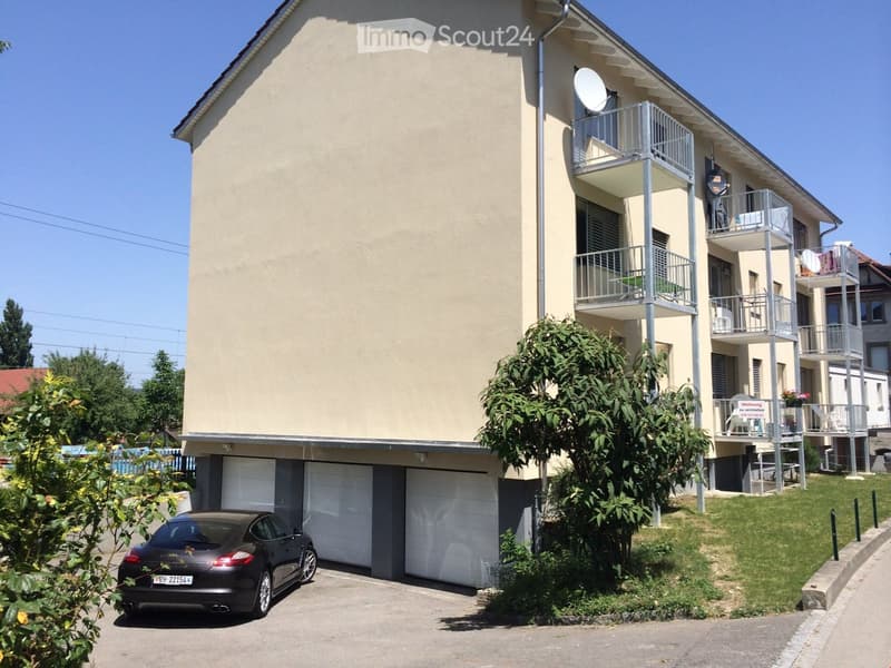 apartment building with three garages, balcony on the upper floors, car parked in front