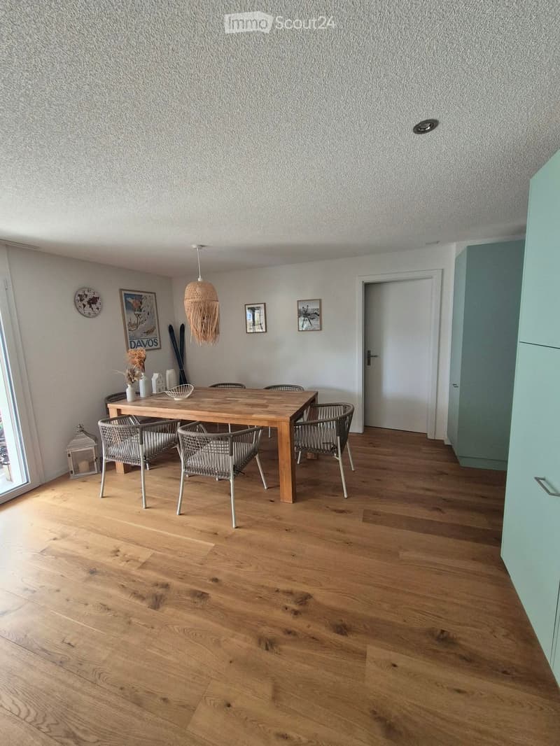 Dining area with wooden floor, dining table, chairs, decorative vases, picture frames, and a wicker hanging lamp.