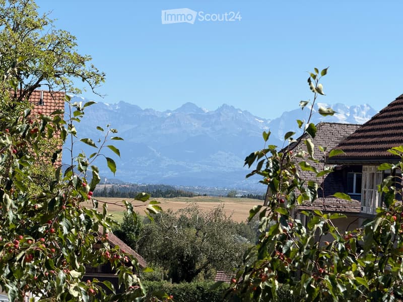 Scenic outdoor view with mountains in the background, houses, trees, and a clear blue sky.