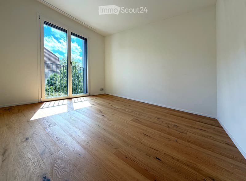 Empty room with light wooden flooring and white walls, featuring a large sliding glass door leading to a balcony.