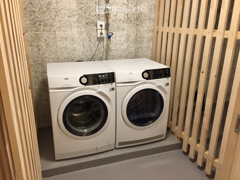 Modern bathroom with a white washing machine and dryer, wooden paneling, and textured wall.