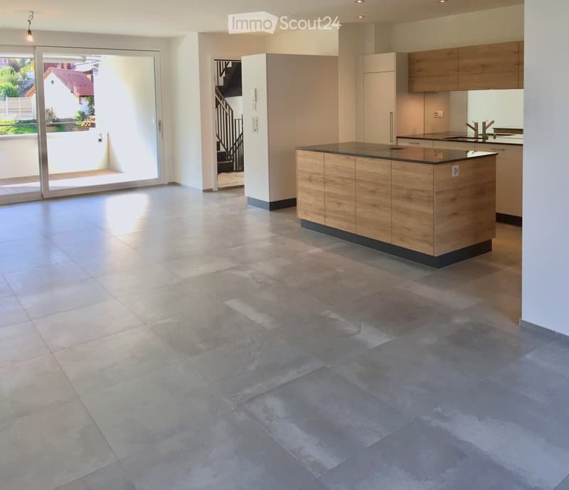 Open-plan kitchen and living area with tiled flooring, modern wooden island, built-in cabinets, and large sliding glass doors leading to a balcony.