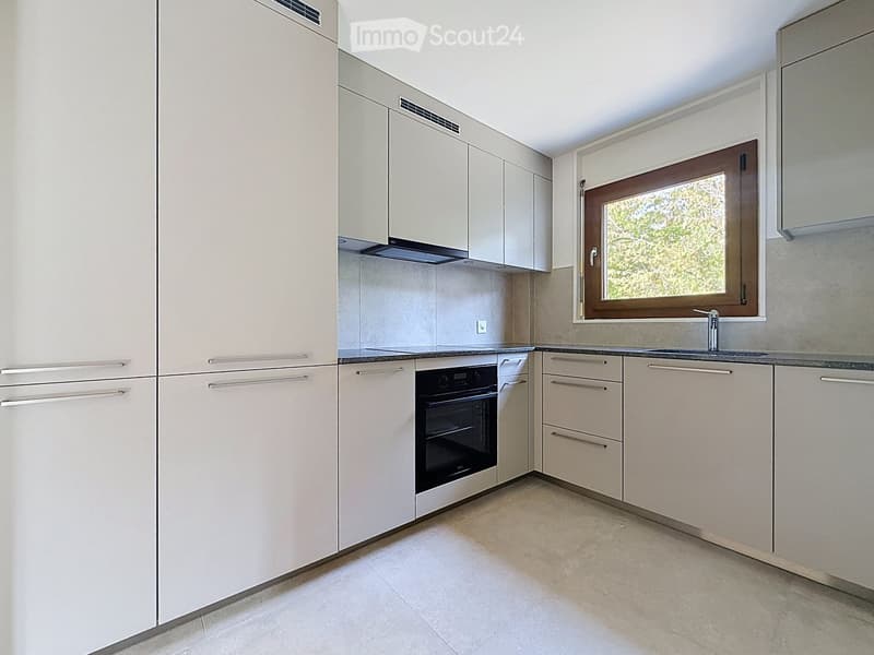 Modern kitchen with light-colored cabinets, stainless steel appliances, and a window overlooking greenery.