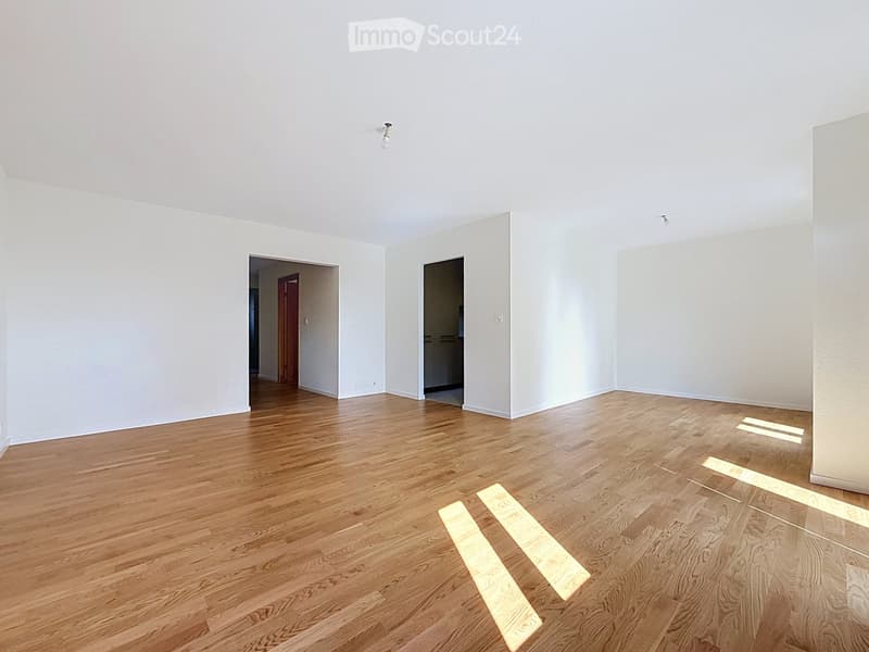 Empty room with light-colored walls and wooden flooring, featuring two doorways leading to adjacent spaces.